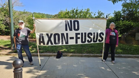 Ken Jones, left, and Melody Shank hold a banner protesting the technology companies that would supply the Asheville Police Department's real-time intelligence center.