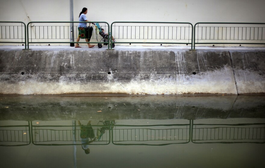 A woman pushing a baby buggy is reflected in a monsoon drain on Friday, Oct. 12, 2012, in Singapore.