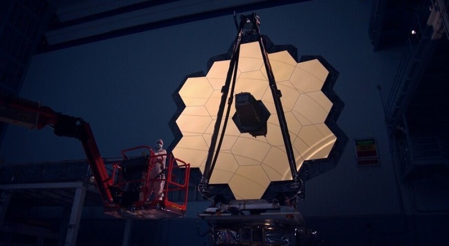 The James Webb Space Telescope's primary mirror is illuminated inside a darkened clean room. The entire telescope is now packed inside a rocket, awaiting launch.