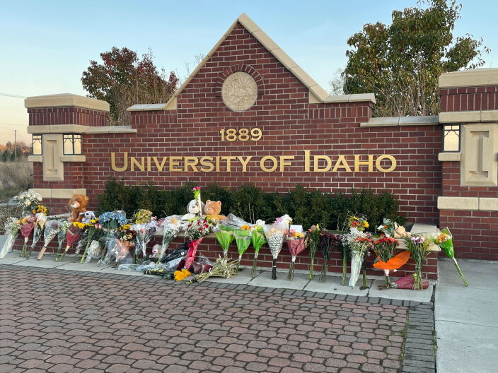 Bouquets of flowers sit on the ground in front of the red brick University of Idaho sign.