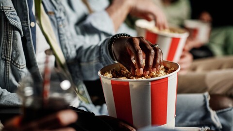 Unrecognizable Black man eating delicious popcorn while watching movie at cinema, selective focus shot
