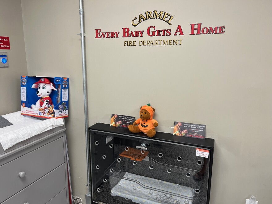 A box where a baby could be safely surrendered under a wall decal that reads "Carmel Fire Department: Every baby gets home." 