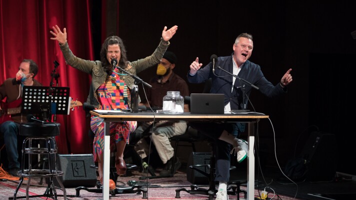 Two podcast hosts on the stage in front of their microphones. 