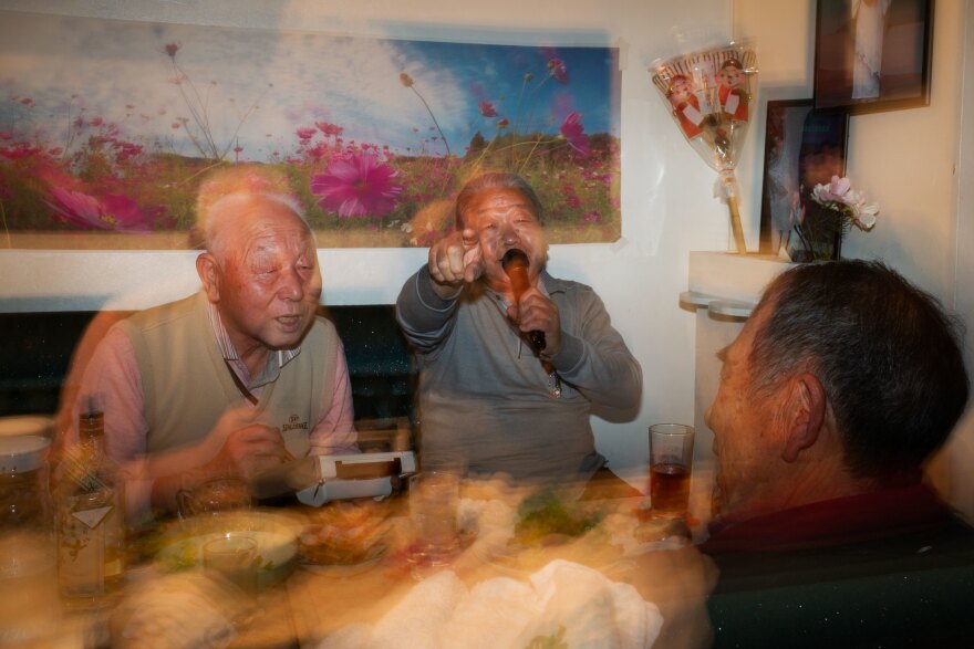 Masato Yamazaki (left) chats with a friend while selecting the next song to sing; Shigeo Kobayashi belts out lyrics at Cosmos Karaoke. The friends try to meet up as often as they can and remember the lives they once had together in Namie.