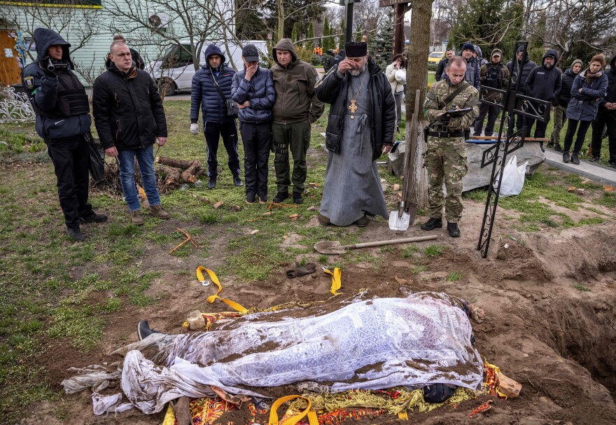 A priest and relatives on Tuesday stand near the exhumed body of Gostomel's mayor, Yuriy Prylypko, who had been buried near a church in the village in the Kyiv region. Prylypko, 62, was killed on March 7 after Russian forces rolled into his village.