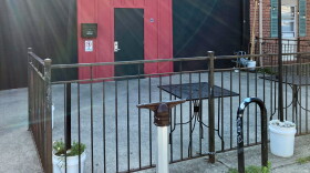  A sign post sits in front of a fenced-in patio at a music all. 