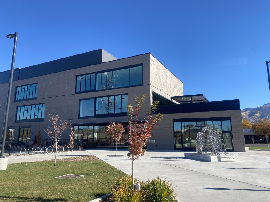 A large building with lots of windows, a smaller metal scuplture sits to the lower right and mountains can be seen in the background, to the right of the building 
