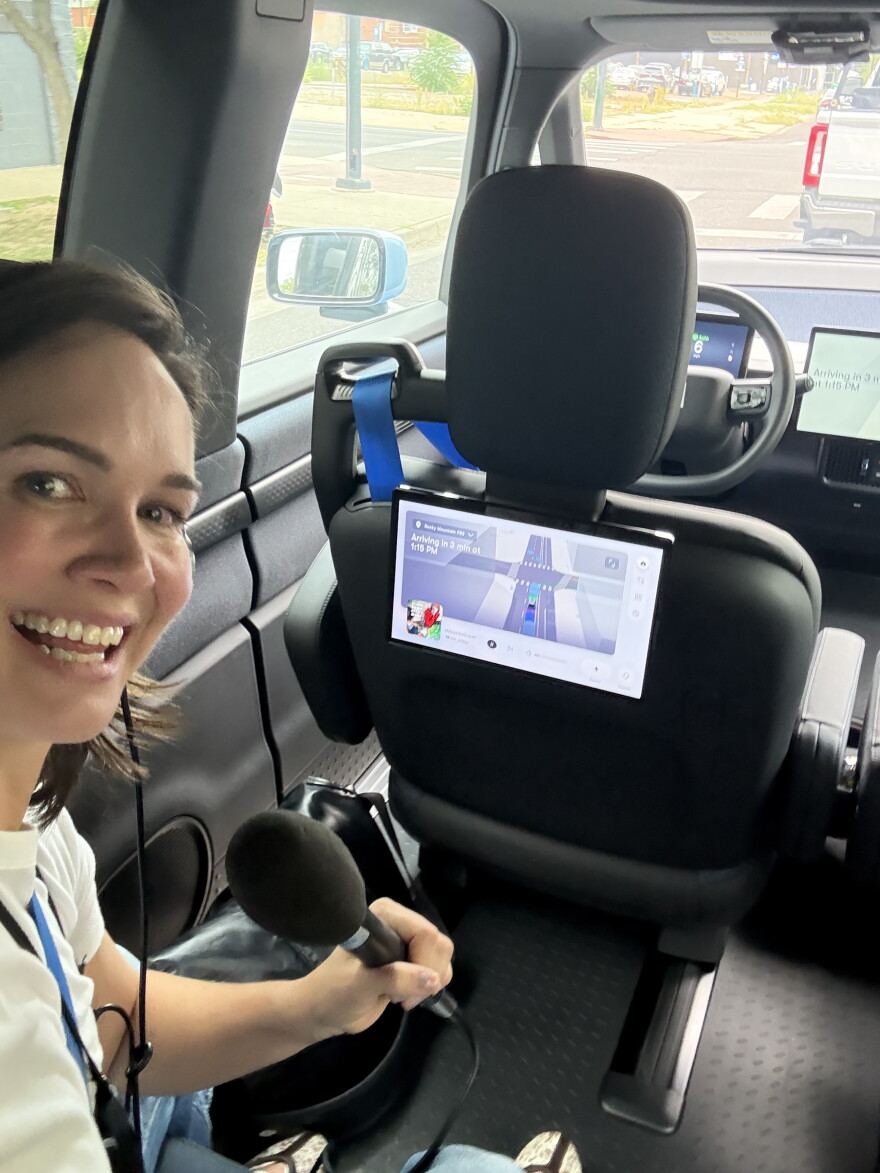  A woman sits in a car, holding a microphone.
