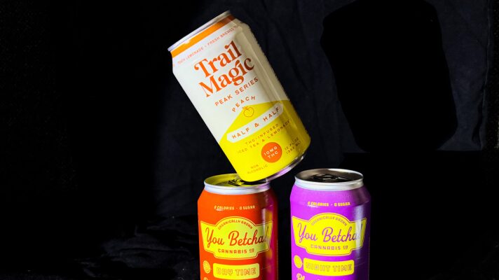 Three cans of THC-infused drinks are stacked on one another in front of a black background.