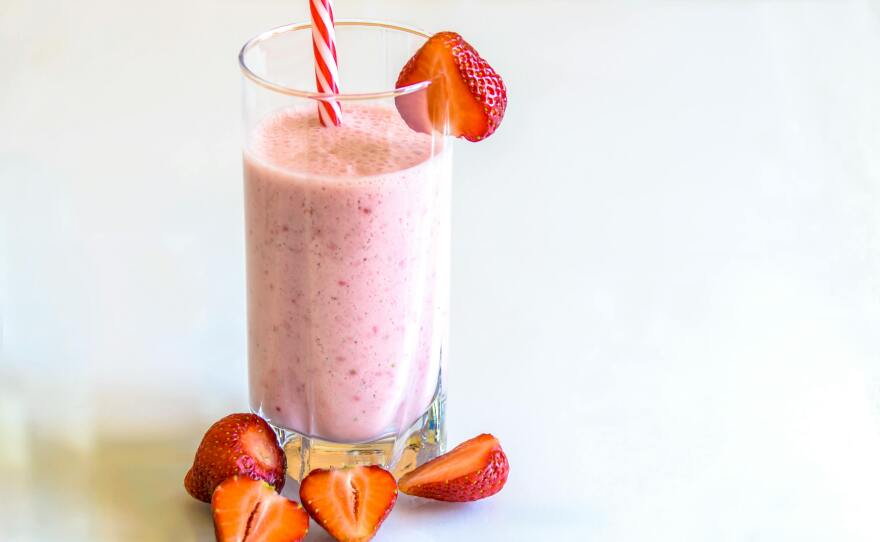 A strawberry shake in a glass, surrounded by more strawberries.