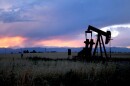 An oil pumpjack in a grassy field with mountains at sunset in the background