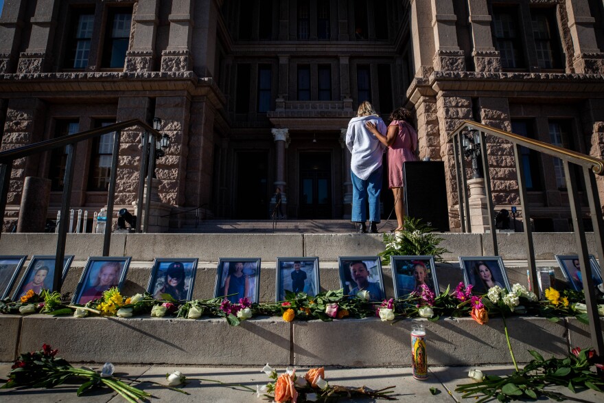 A person puts their hand on the back of another person near photos, flowers and candles on the steps of the Capitol.