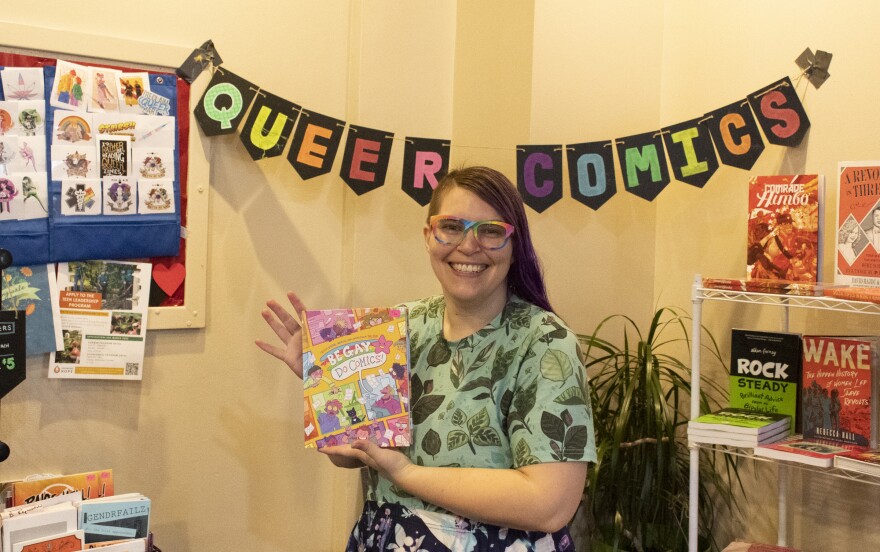 Amara Vear, founder of Queer Comics Peddler holds a comic up at their pop-up shop.