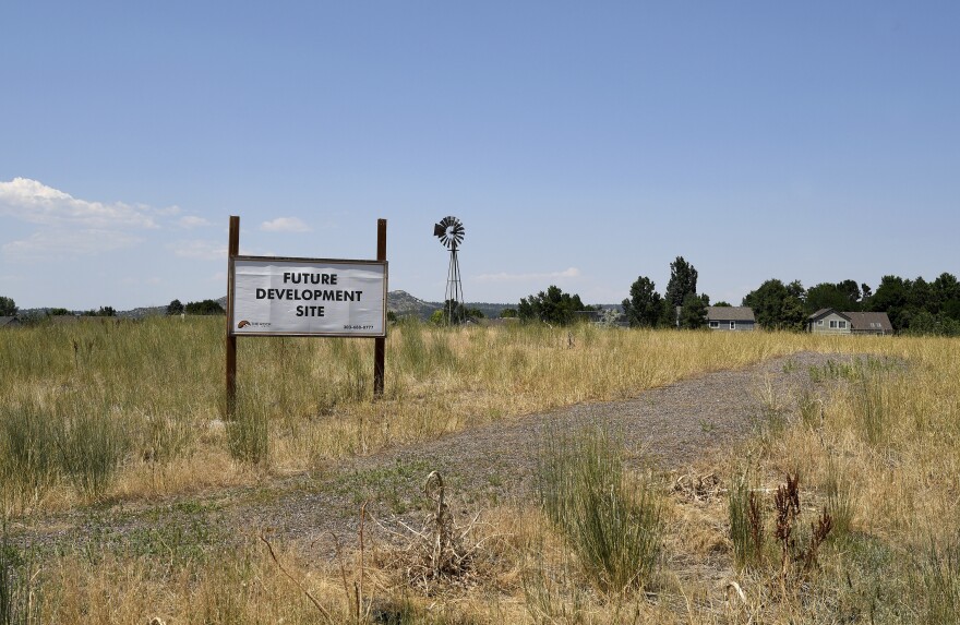 A sign saying "future development" sits in a field with houses in the distant background.