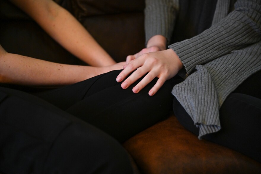 Partners Lydia Bennett, left, and Anna Porter, right, hold hands while sitting on Porter’s couch on Tuesday, April 2, 2024, at Porter’s apartment in Columbia.