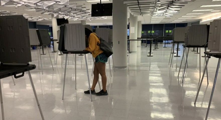 a woman in an otherwise empty polling place leans into a voting booth 