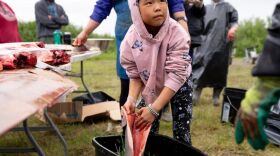 a girl holds a fileted salmon near a tote, outside