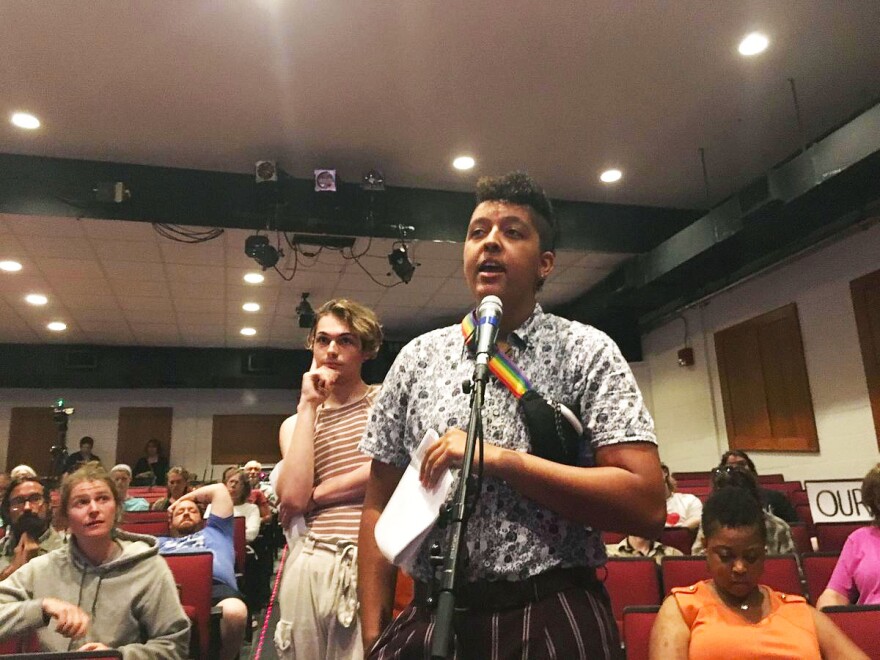 A person stands before a microphone in an auditorium.