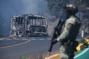 FILE - A soldier stands guard by a charred vehicle after it was set on fire