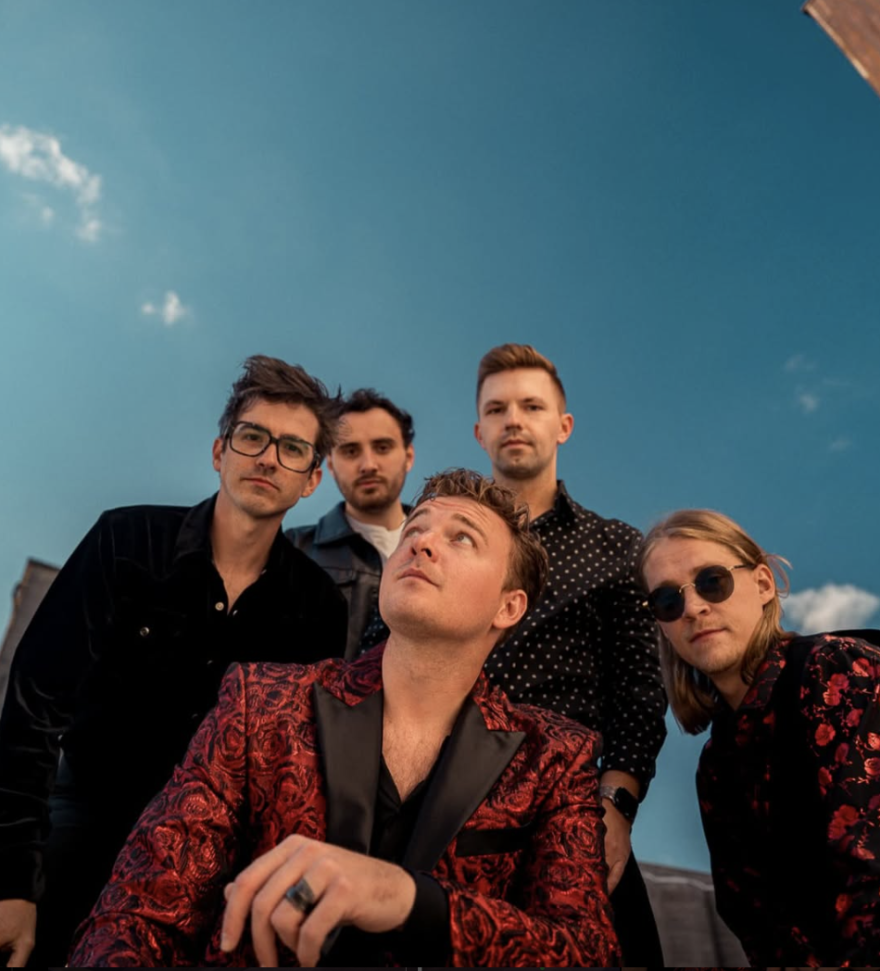 camera is on the ground, pointed towards the sky. the band is learning over, all but one looking down at the camera