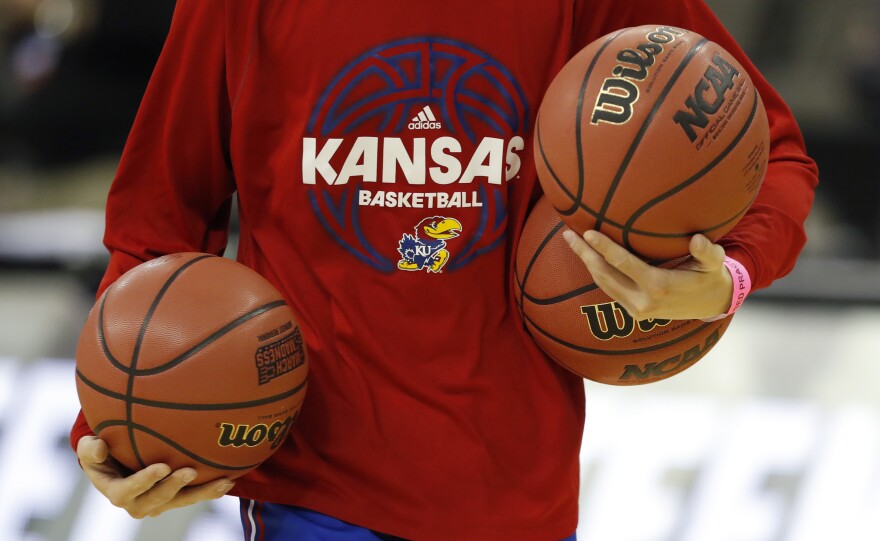 A Kansas team manager carries basketballs during practice at the 2018 NCAA men's college basketball tournament in Omaha. The team was forced Wednesday to vacate its appearance in the tournament, over bribery and recruiting violations dating back to 2014.