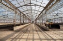 What looks like a large, glass-paneled greenhouse, except the class is uncolored and clear. The sludge at this distant just looks like dirt spread across the floor. To the right is a yellow and black front loader construction vehicle.