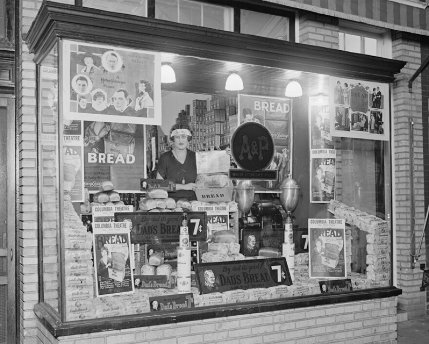 A woman stands in the bakery window of an A&P storefront, 1924.