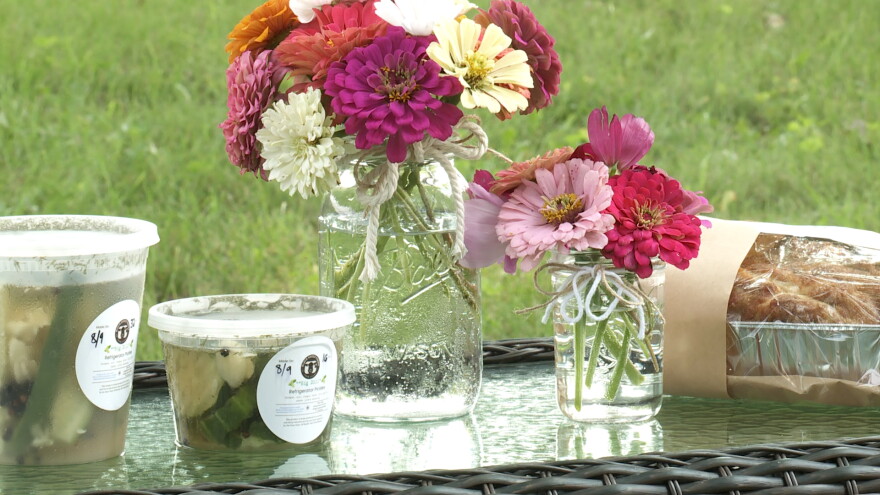 A vase of flowers and a jar of pickles on a table.