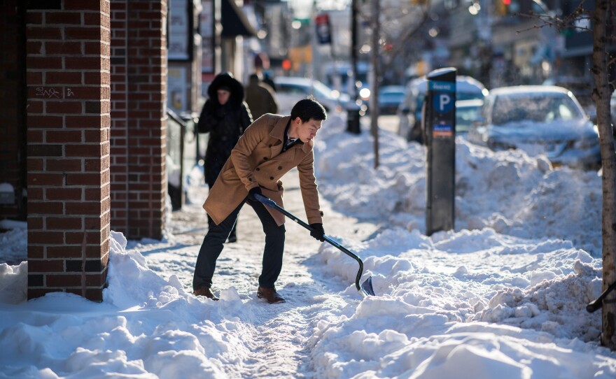 A man shovels snow from a footpath in New York City.