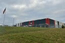 Photograph of L&M Fleet Supply distribution center with building, yard, fence, cars, and an American flag