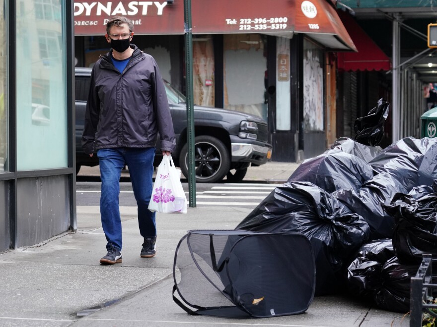A man wearing a protective mask looks at piled-up trash in New York City on April 24. Cities are struggling with collection as the volume of residential garbage surges during the stay-at-home era. [Cindy Ord / Getty Images]