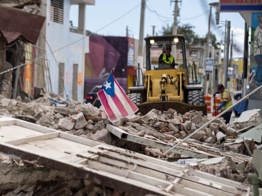 A Puerto Rican flag waves on top of a pile of rubble as debris is removed from a main road in Guánica.