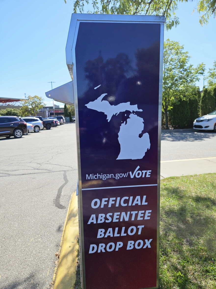 A Michigan ballot drop box stands in the grass next to a parking lot.