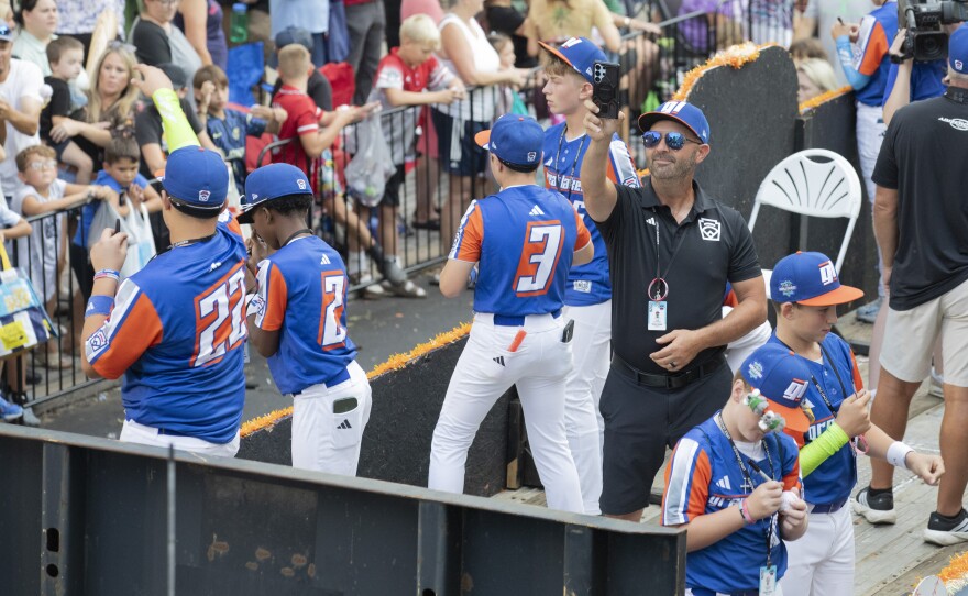 Ken Coomer, coach of the Great Lakes region team, captures the scene from his team's float in the Little League World Series parade.