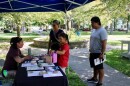 A man and woman with their two children speak to a mental health advocate at a book, outside in Frankline Park.