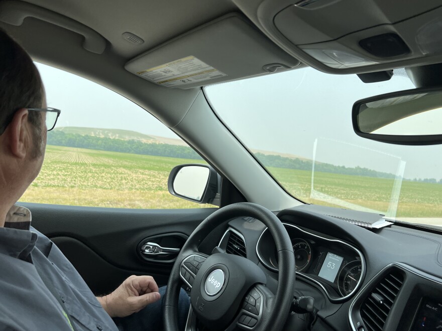 A man with glasses looks out a car window while driving. He is looking at the hills of Sunny Farms Landfill.