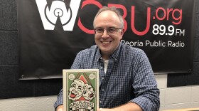 Bradley University Associate Professor of Theater Arts Travis Stern holds a copy of his book "Ballplayers On Stage" as he sits in front of the banner in the WCBU master studio in Peoria. 