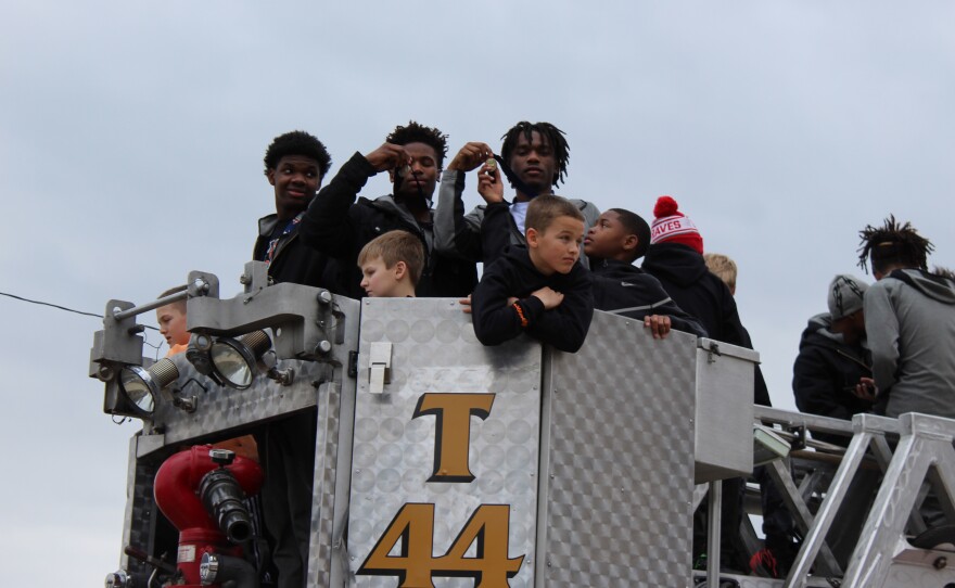 Two Manual High School basketball players show off their medals on the top of a firetruck.