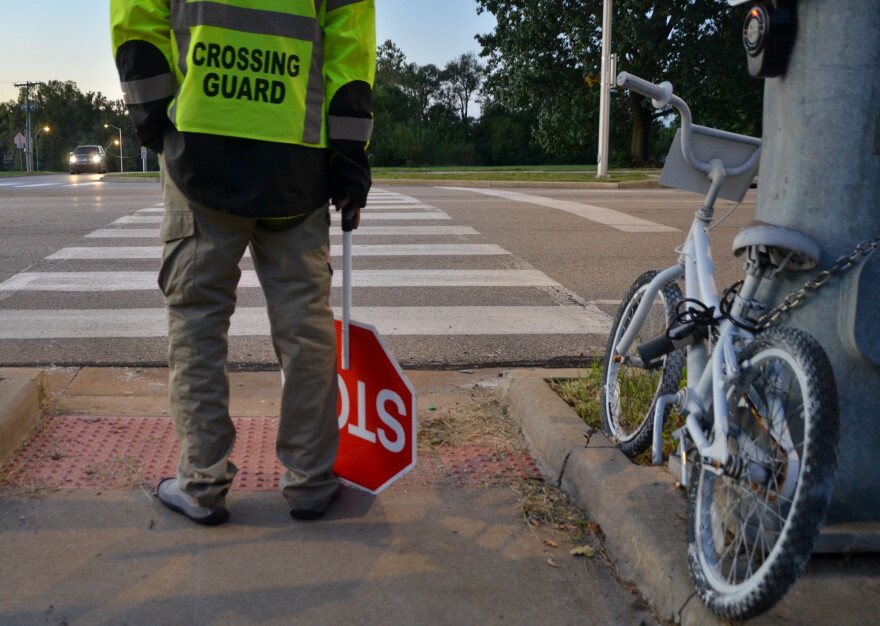 A crossing guard stands at Food Lane and Longview Road, next to a bike memorializing Hazen Workman-Duffy who was fatally struck by a car while on her way to school a year ago.