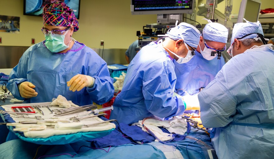 From right, Dr. Kiran Dhanireddy, Dr. Diego Reino and Dr. Ashish Singhal in hospital scrubs, masks, gloves, and glasses. They're standing over a patient on the operating table.