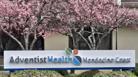 A sign reading "Adventist Health Mendocino Coast" underneath trees with pink blossoms.