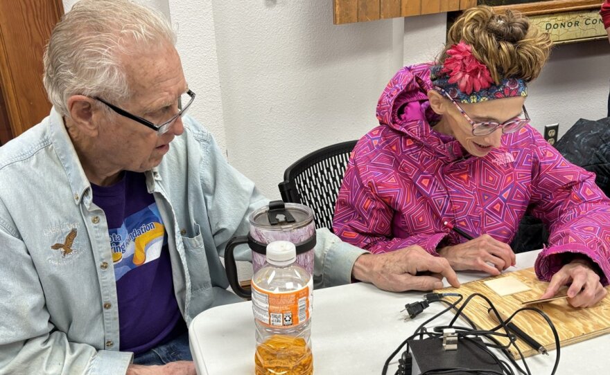 A man wearing a blue button up helping someone in a pink coat woodburn