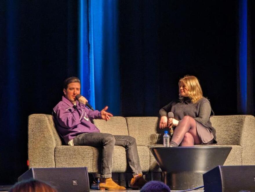 Logan Henderson answers a question, while holding a microphone, seated
