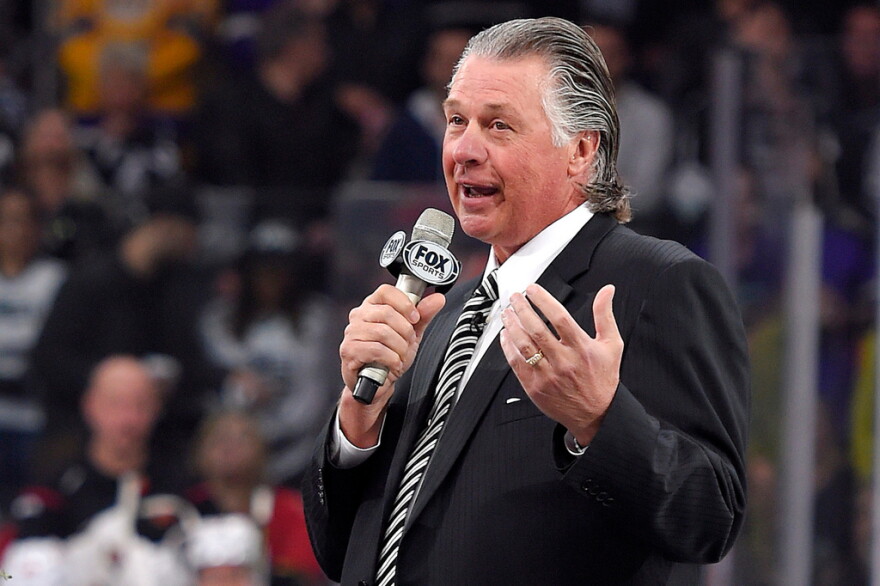   Barry Melrose speaks to fans holding a microphone at an arena