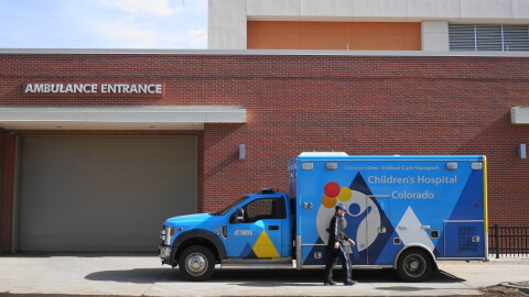 A first responder walks in front of a blue ambulance that's parked outside of a hospital emergency room.
