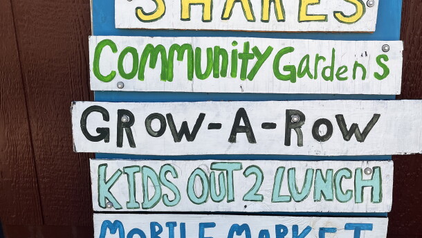 Colorful sign listing program offerings of a food program including "shares" "grow-a-row" and "composting"