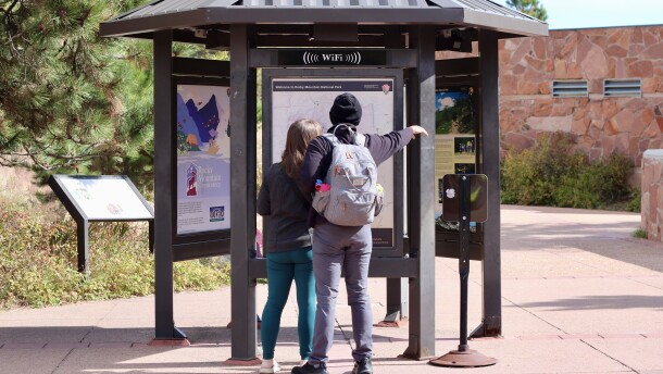 Two people facing away from the camera are looking at a sign of the national park map.