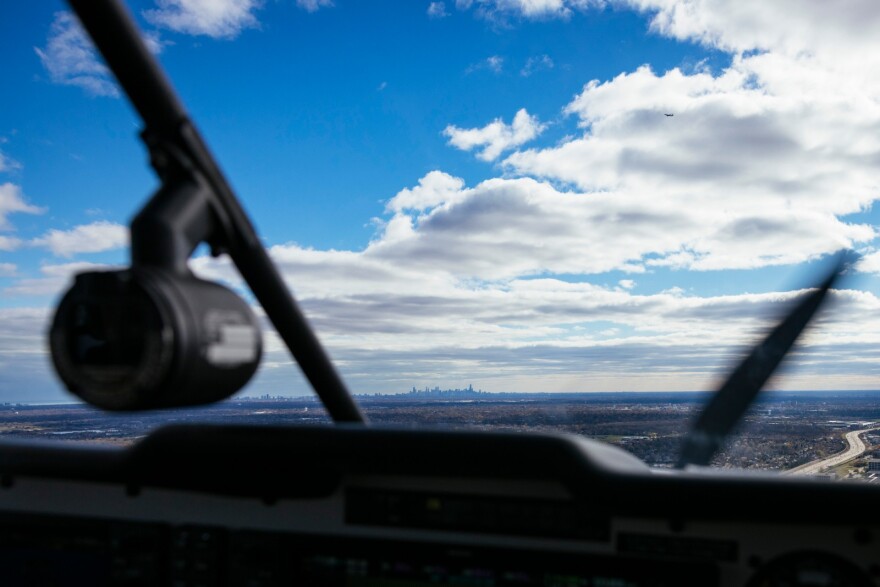 A wide, horizontal view of the sky ahead from the windshield of an airplane's cockpit. The Chicago skyline sits in the distance on a recent flight piloted by an Elevated Access volunteer.