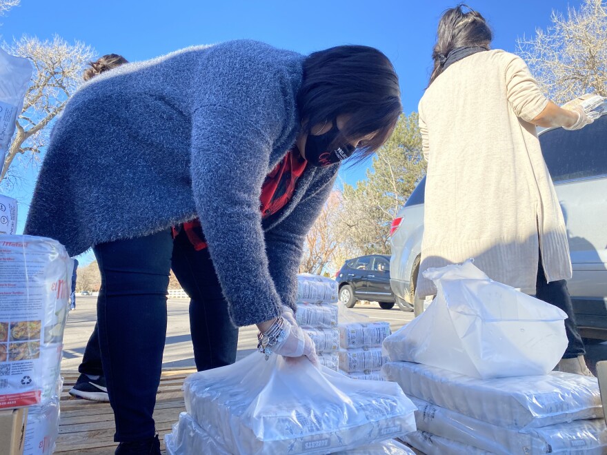 A woman opens a bulk package of food on a pallet in a parking lot.