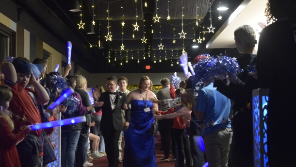 two people walk down a red carpet with two vertical parallel lines of people cheering
